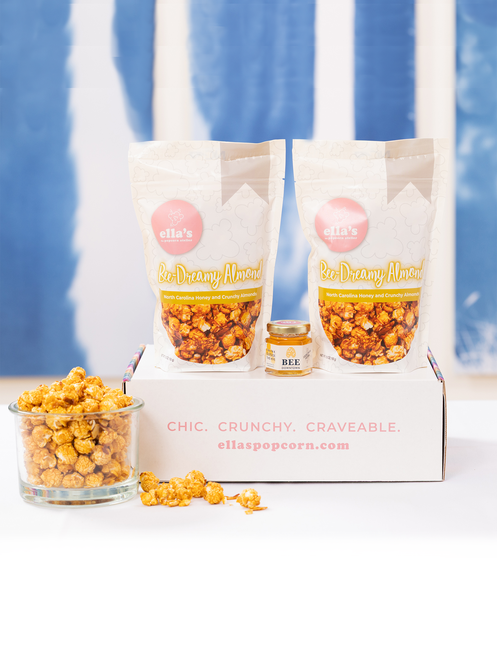 Popcorn packaging with a glass container of popcorn, a jar of honey, and a blue curtain background