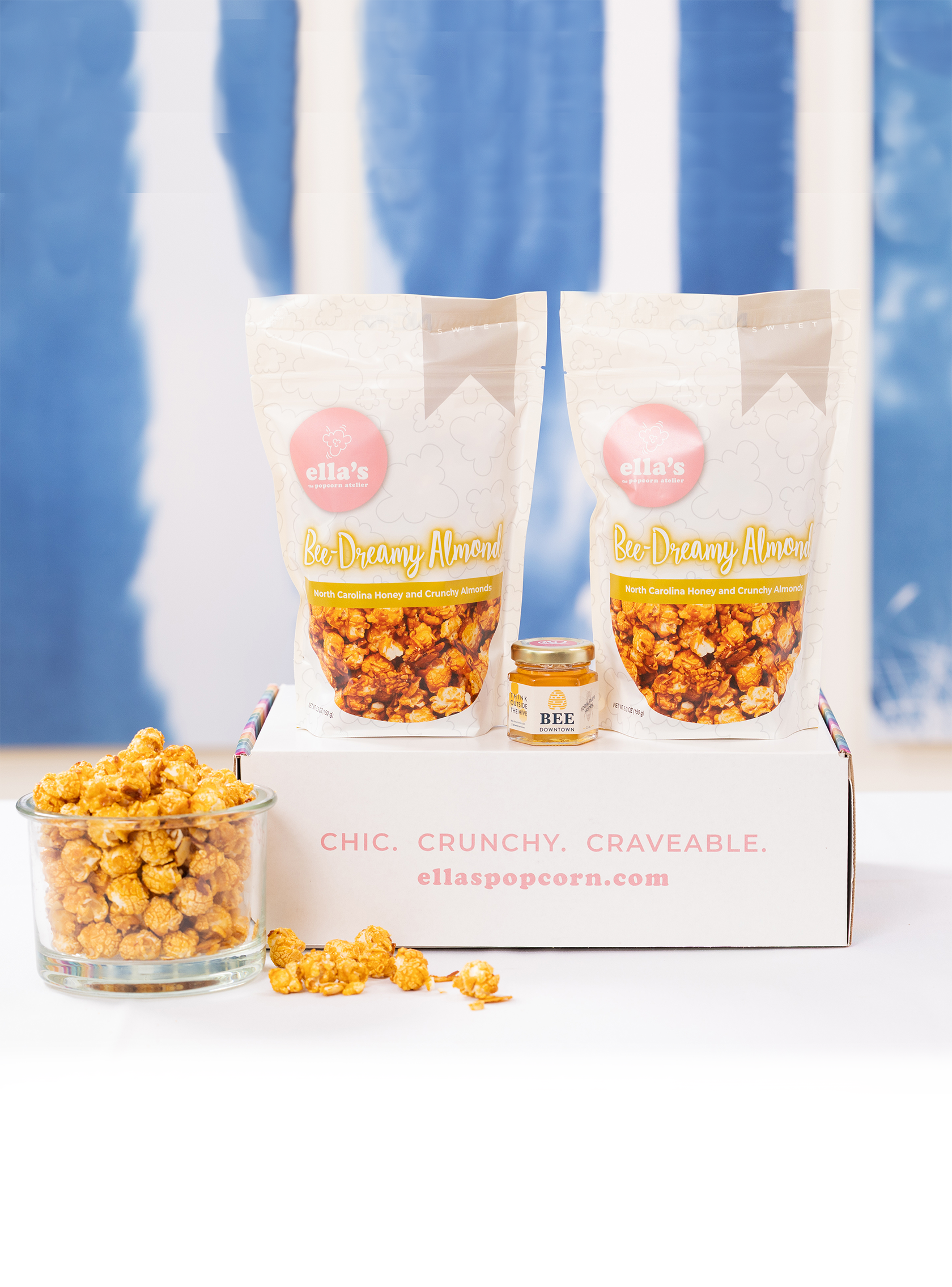 Popcorn packaging with a glass container of popcorn, a jar of honey, and a blue curtain background